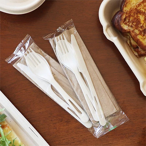White compostable cutlery sets on a wooden table.